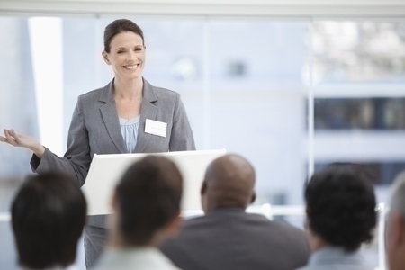 Smiling businesswoman gesturing with her hand as she is being watched by her colleagues with focus on the businesswoman