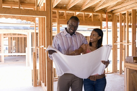 Young couple looking at blueprints in partially built house, smiling