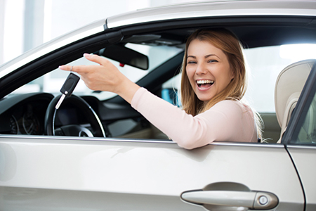 Cheerful woman sitting in a car holding new car keys.