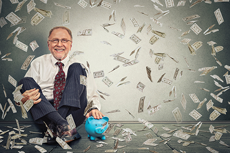 Excited happy senior man sitting on a floor with piggy bank unde